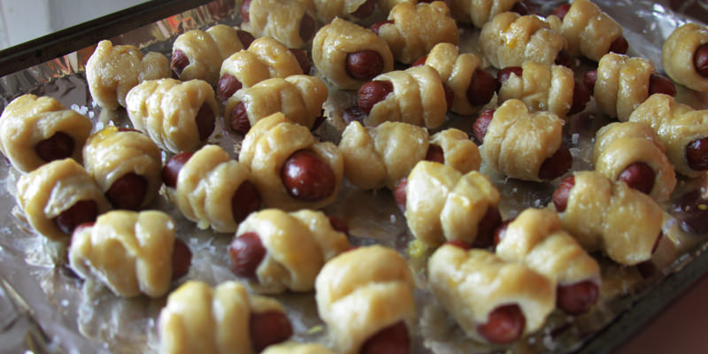Freshly basted beer-pretzel wrapped pigs-in-a-blanket ready for the oven.