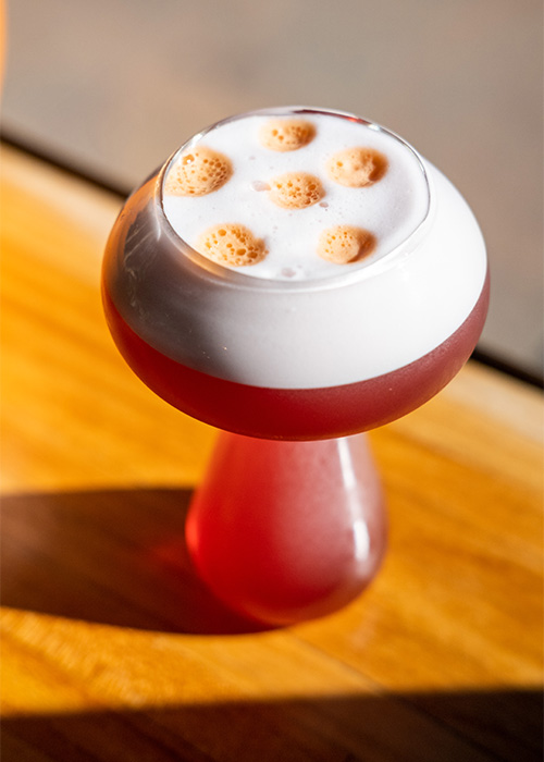 Shitake Happens is a cocktail served in a mushroom-shaped glass that has bitters resting on top in the shape of dots. 